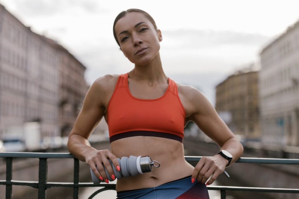 Woman wearing a red spots bra leaning on a rail. She is holding a waterbottle in her left hand