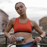 Woman wearing a red spots bra leaning on a rail. She is holding a waterbottle in her left hand