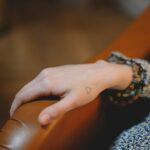 A small heart tattoo on the side of a person's hand, sitting on the edge of a couch.