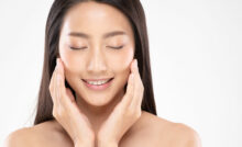 Beautiful Asian young woman smiling and touching her cheeks with her hands with her eyes closed.