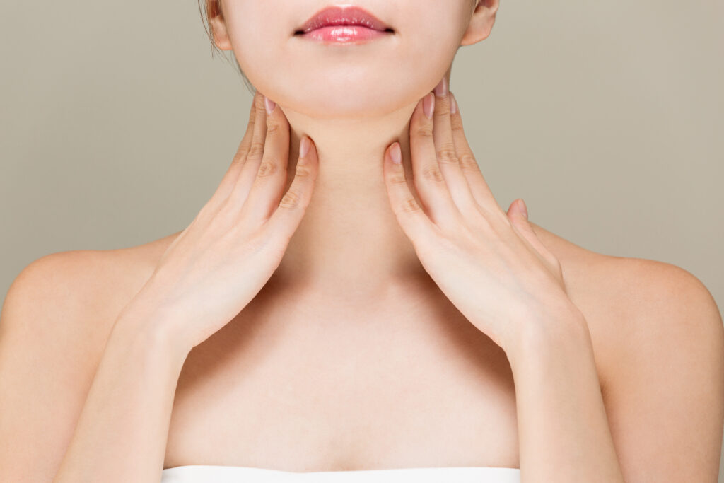 Woman seen from chin down, with hands gracefully placed against her neck.