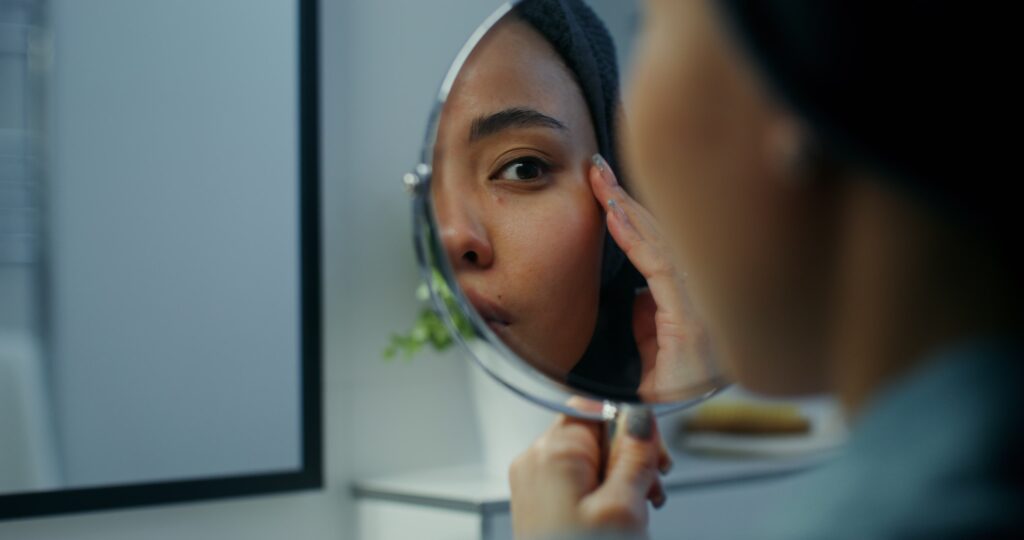 Woman carefully examining her face in a hand held mirror.