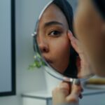 Woman carefully examining her face in a hand held mirror.